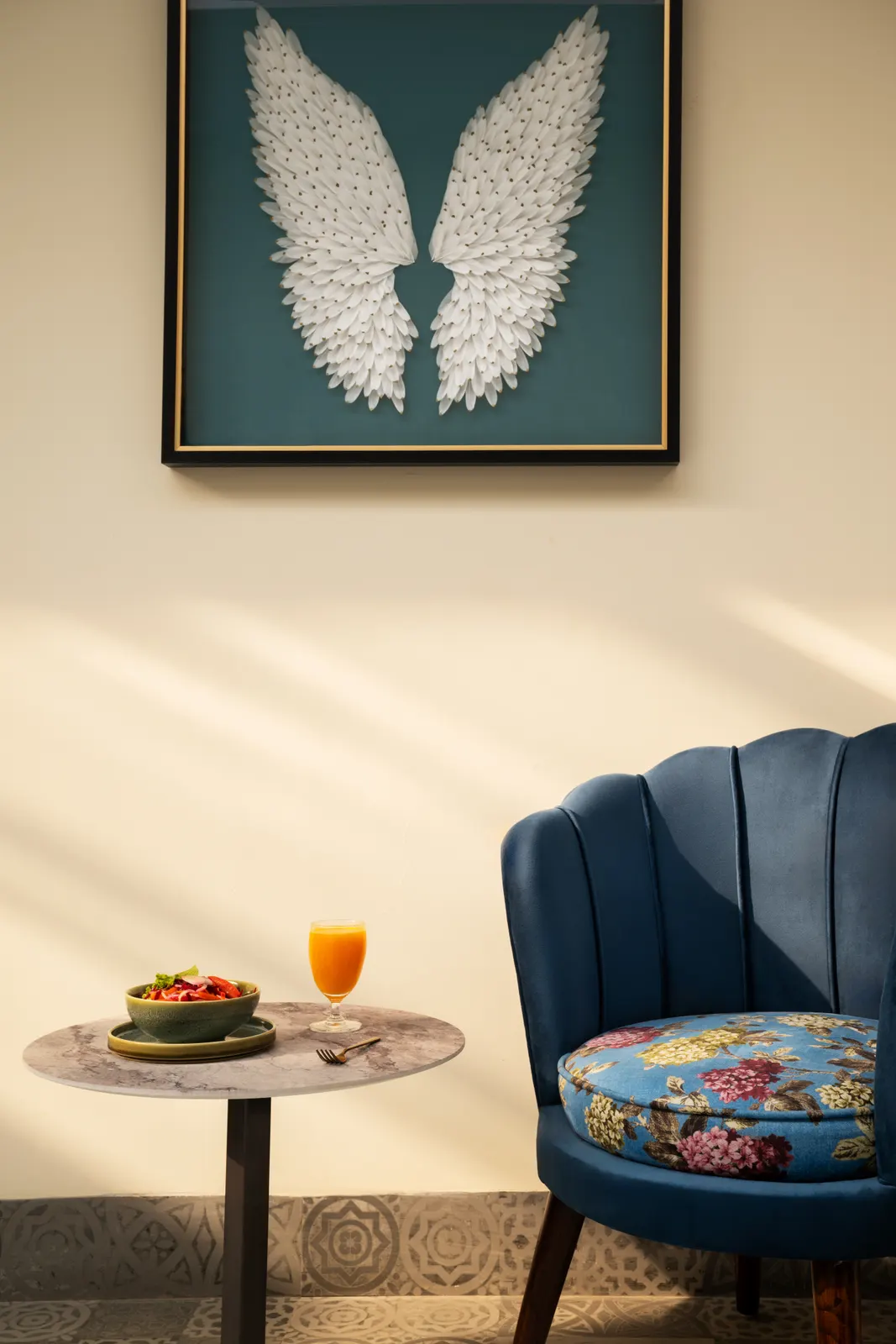 Une chaise bleue, une petite table et une œuvre représentant une plume